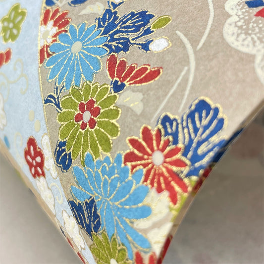 japanese silk-screen handmade paper showing taupe and pale blue waves pattern with multicolour flowers and foliage, with gold accents, close-up