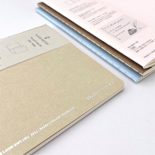 Soft cover notebook with grid format pages. Cover is plain beige with branded belly band, close-up