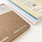 Soft cover notebook with grid format pages. Cover is plain brown with branded belly band, close-up