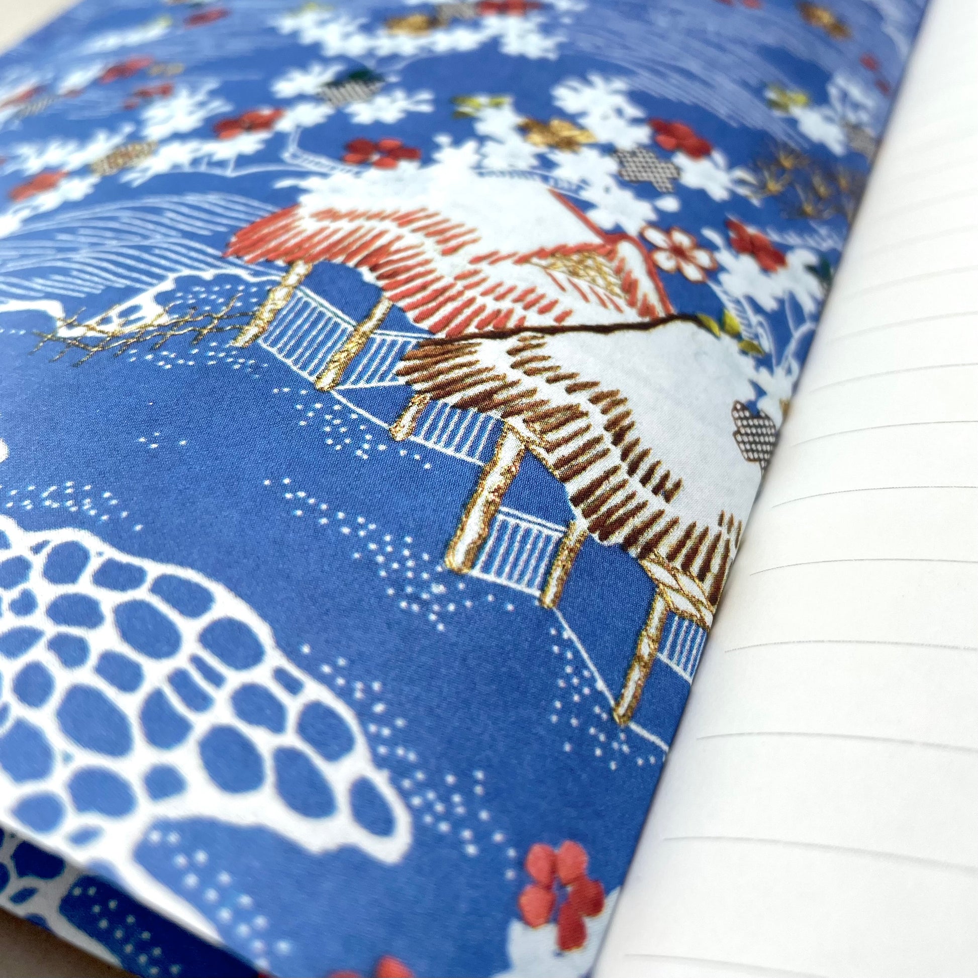 A5 lined notebook with a japanese cover design with white swans on an orange background, close up of the blue endpaper