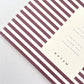 Pocket size notebook with a narrow bordeaux and white stripe softcover. close-up