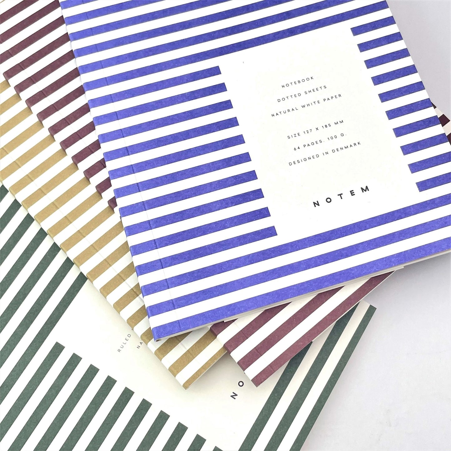 Pocket size notebook with a narrow bright blue and white stripe softcover. pictured with other colour notebooks