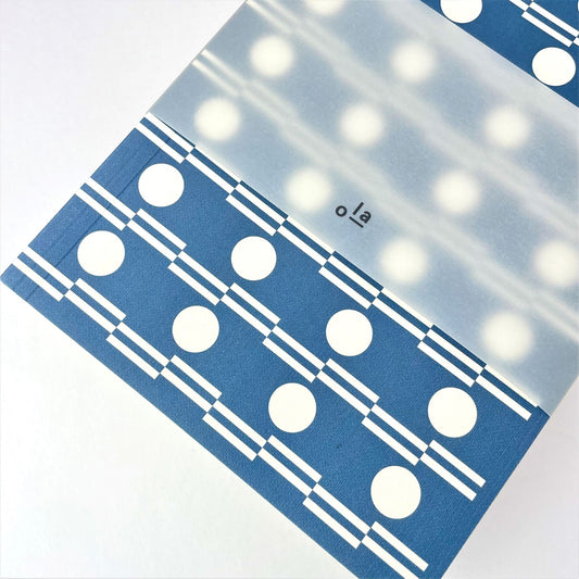 A5 softback notebook with geometric blue and white circle repeat patterned cover. Plain inner pages, pictured with branded belly band