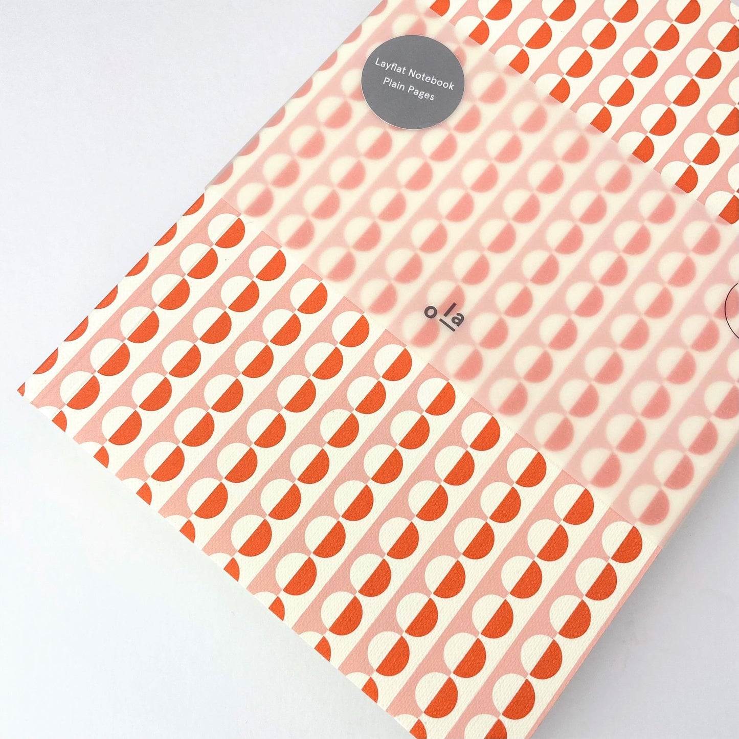 A5 softback notebook with geometric orange and pink repeat circle patterned cover. Plain inner pages, pictured with branded belly band