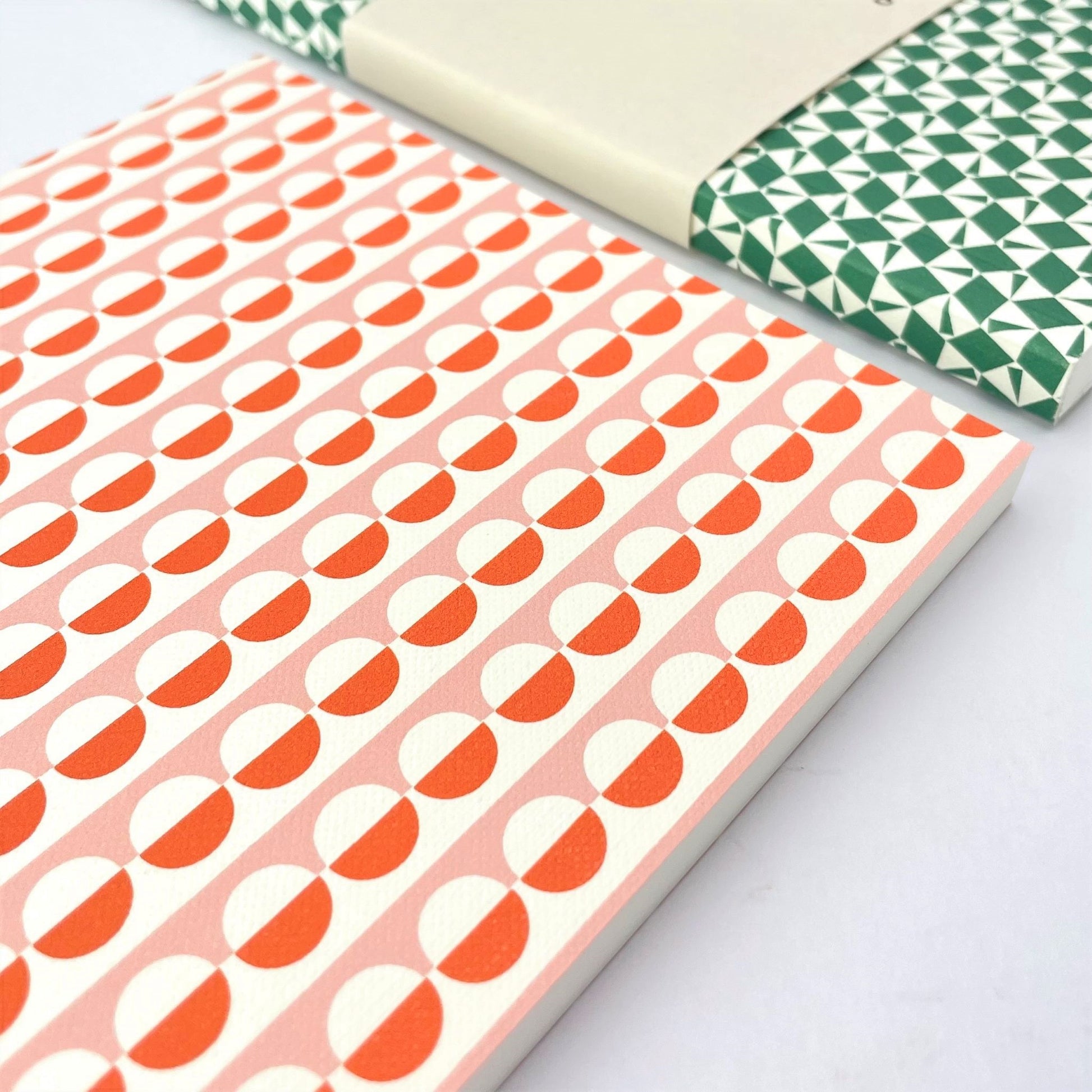 A5 softback notebook with geometric orange and pink repeat circle patterned cover. Plain inner pages, close-up
