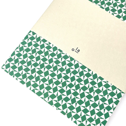 A5 softback notebook with geometric emerald green and white repeat diamond and triangles patterned cover. Dotted inner pages, pictured with branded belly band