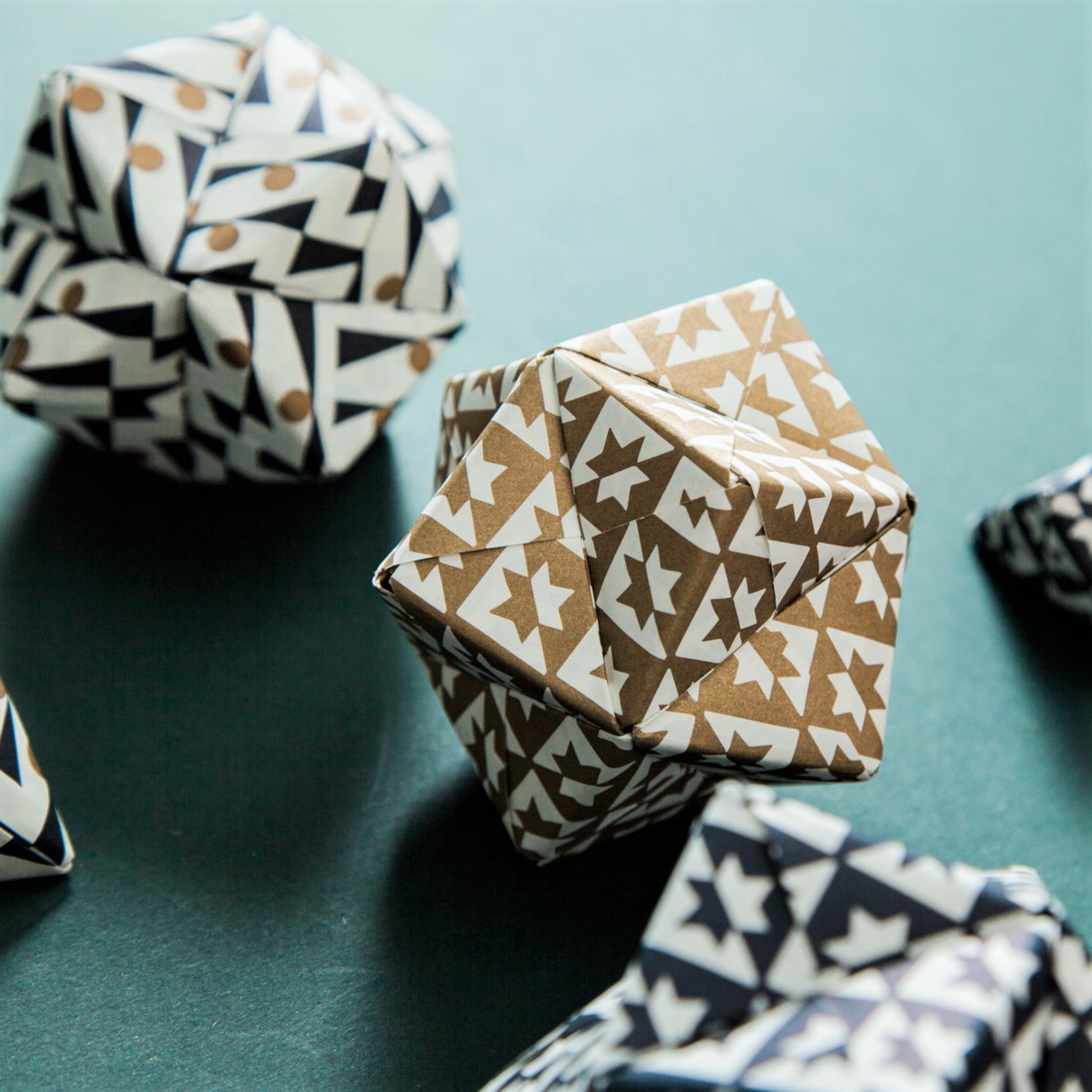 A set of patterned paper origami pyramid and bauble shaped decorations, in colours red, gold, navy and white, close-up of gold paper bauble