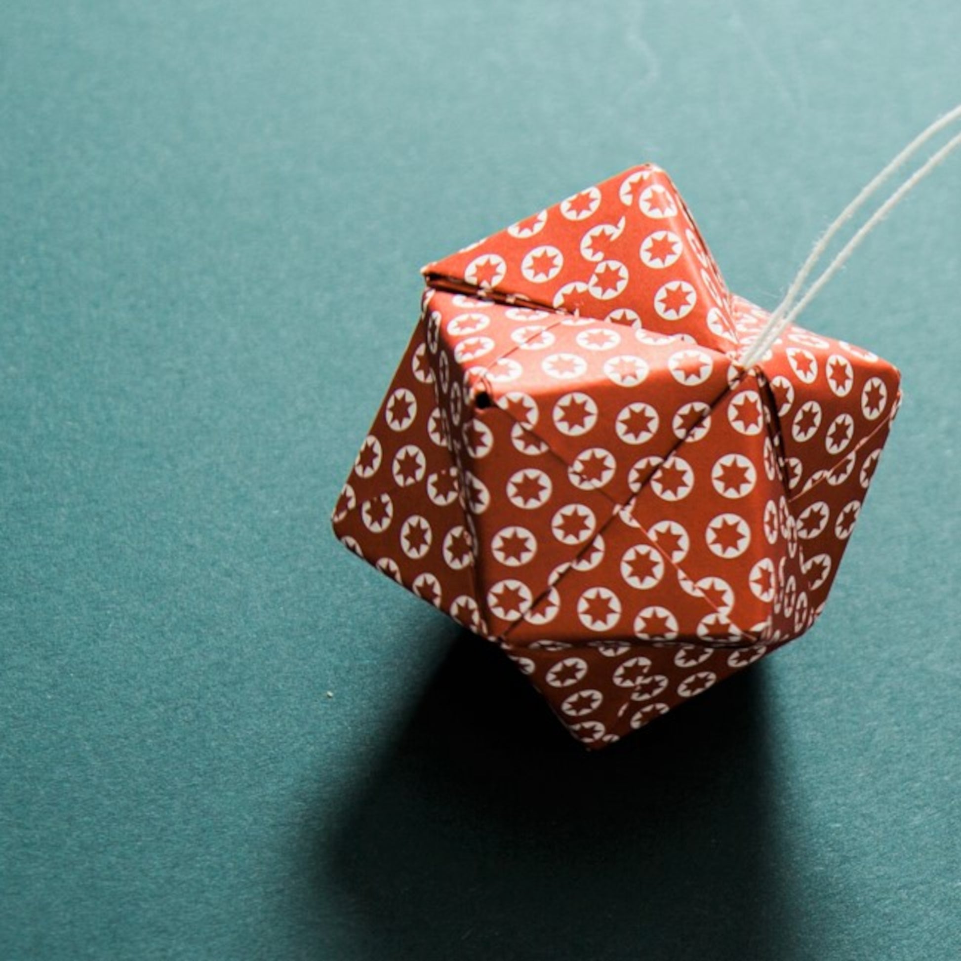 A set of patterned paper origami pyramid and bauble shaped decorations, in colours red, gold, navy and white, close-up of red paper bauble