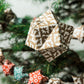 A set of patterned paper origami pyramid and bauble shaped decorations, in colours red, gold, navy and white, close-up of gold paper bauble hung on a christmas tree