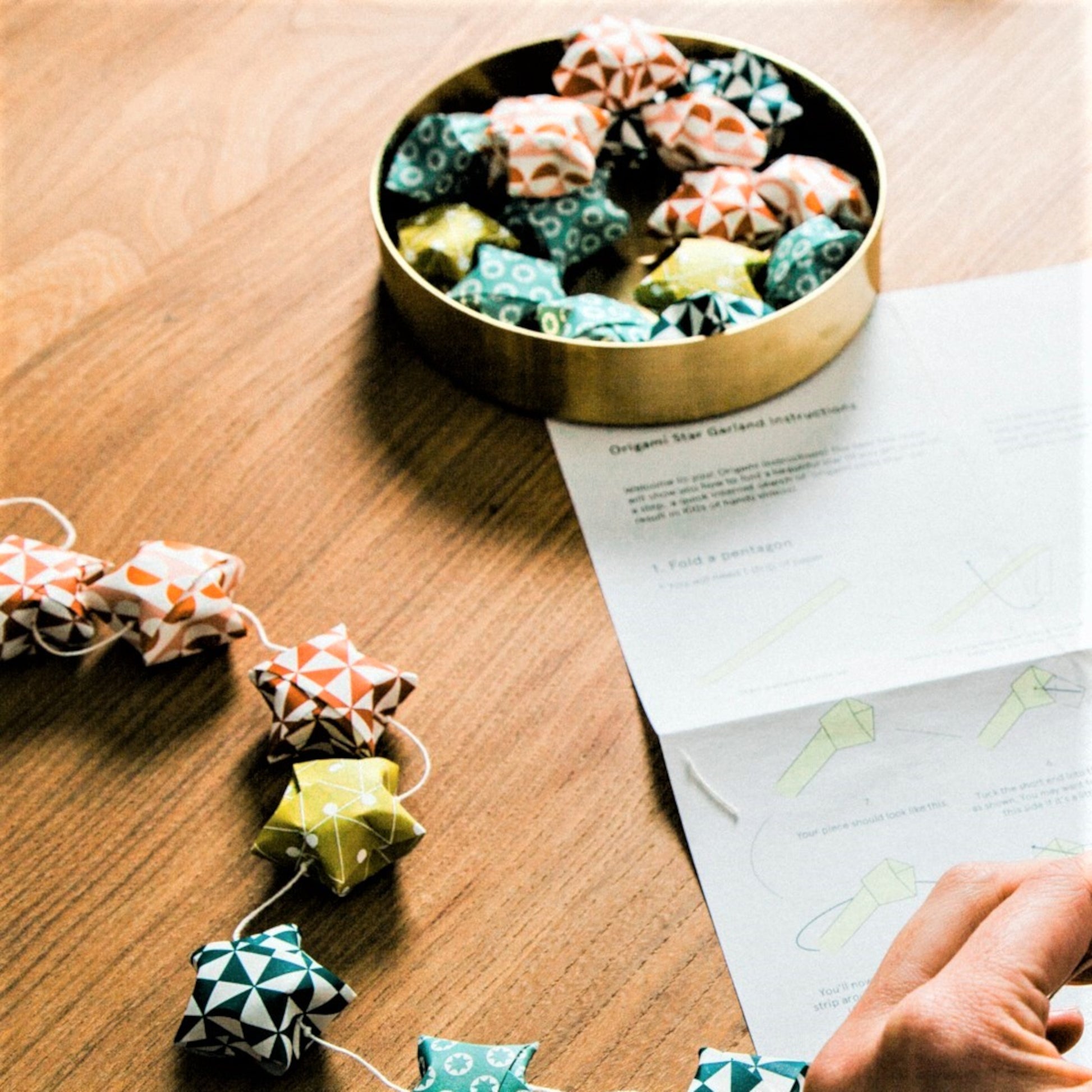 A garland of small paper origami patterned stars "lucky stars" in mustard, teal, aqua and orange, close up of the instructions