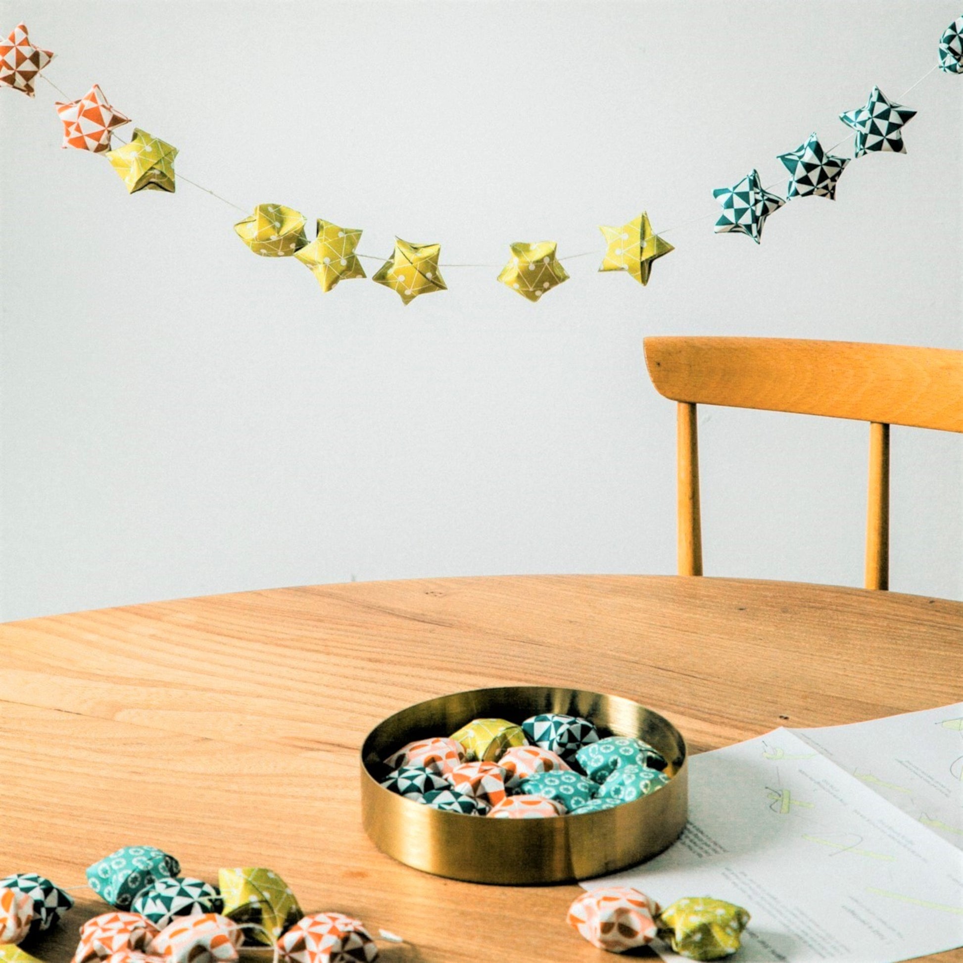 A garland of small paper origami patterned stars "lucky stars" in mustard, teal, aqua and orange, hanging above a table