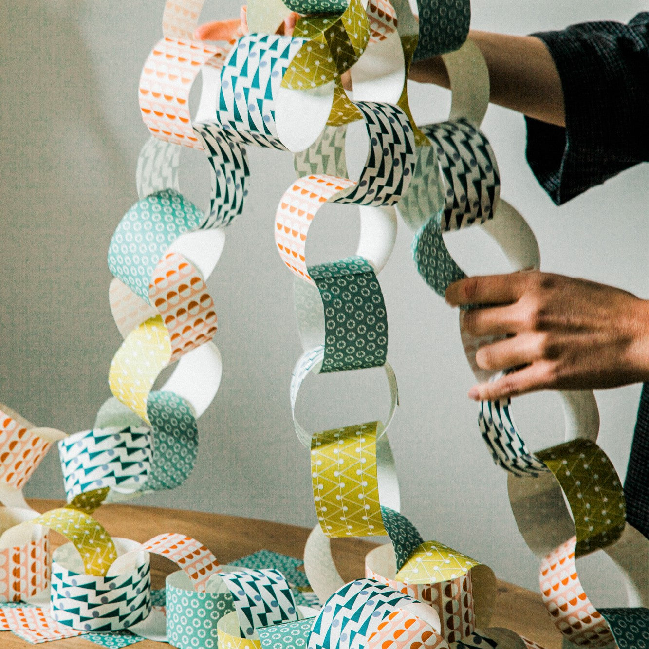 A paperchain of different patterned geometric papers in colours of mustard, orange, aqua and teal, pictured being ready to hang