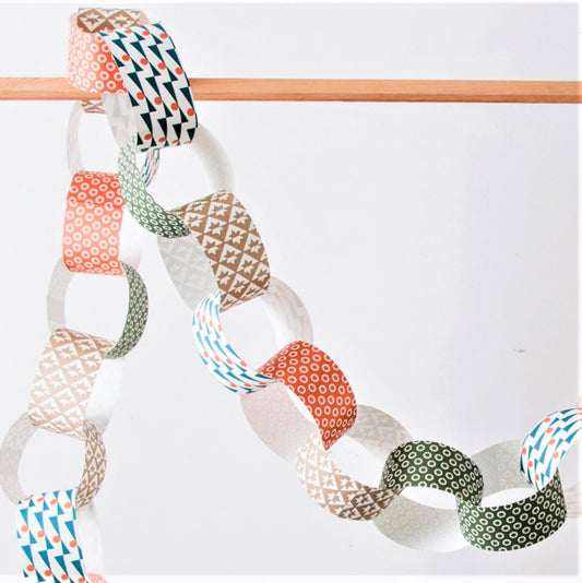 A paperchain of different patterned geometric papers in colours of gold, red, olive and blue, pictured hanging from a pole