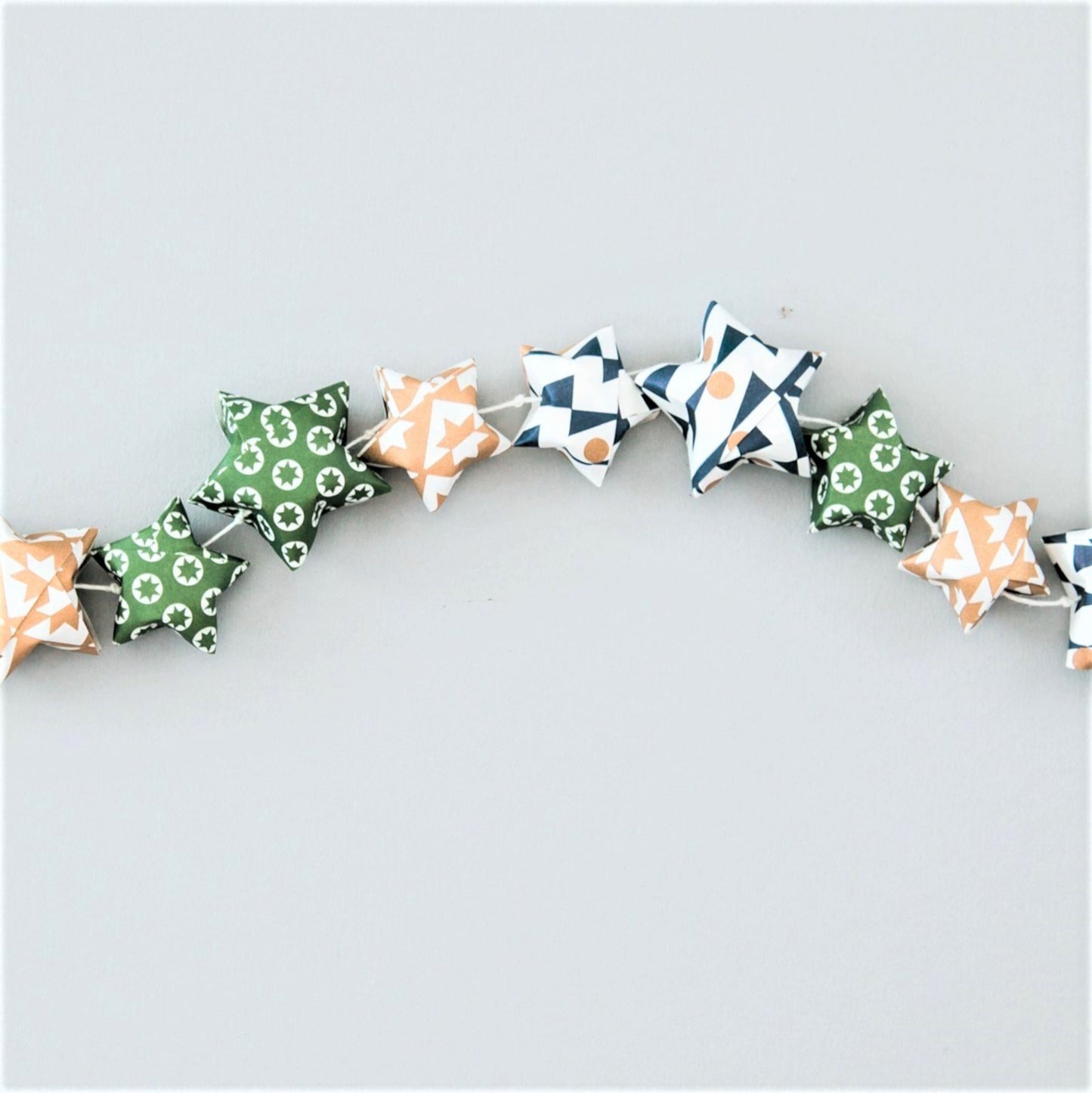 A garland of small paper origami patterned stars "lucky stars" in green, gold and dark blue