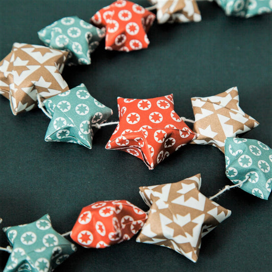 A garland of small paper origami patterned stars "lucky stars" in red, gold and aqua, pictured close-up