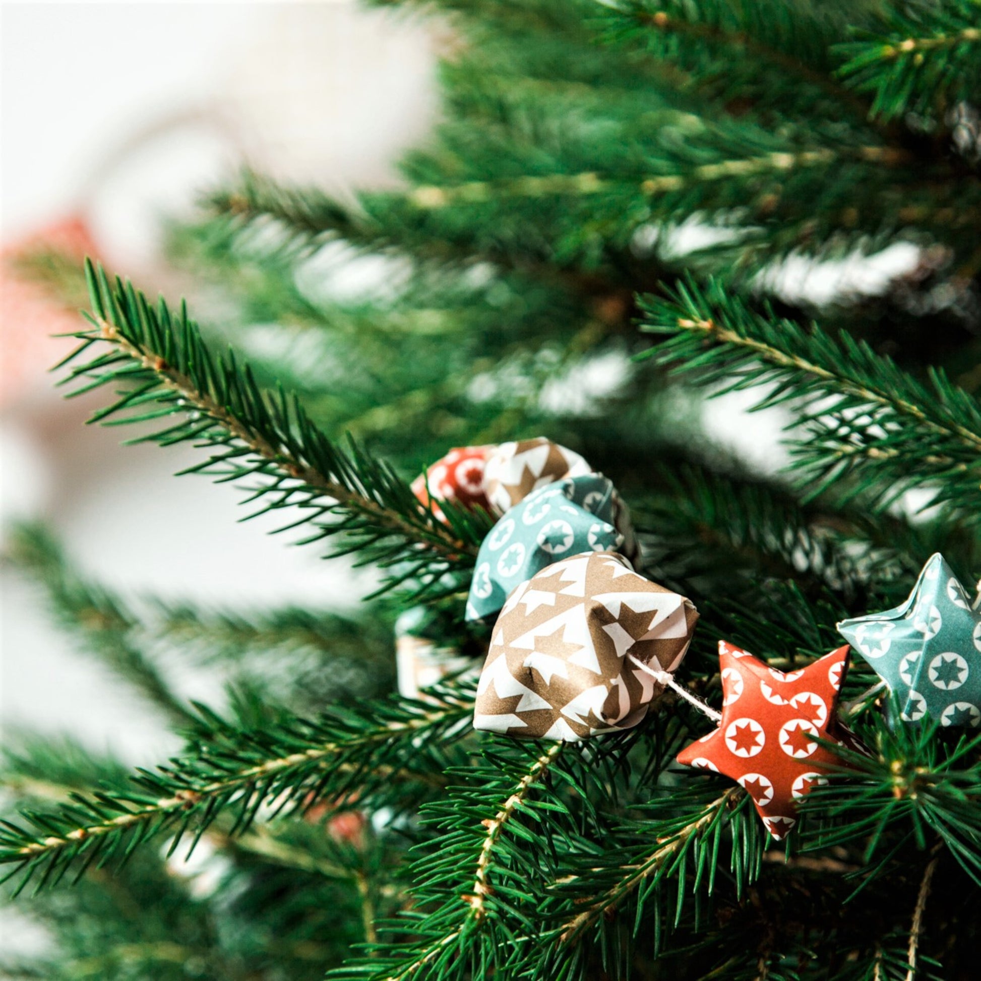A garland of small paper origami patterned stars "lucky stars" in red, gold and aqua, pictured decorating a christmas tree