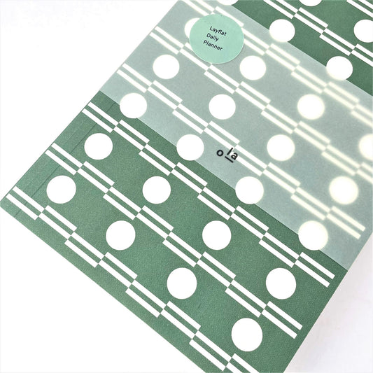 A5 softback 12 week daily planner with geometric green and white circle repeat patterned cover., pictured with branded belly band