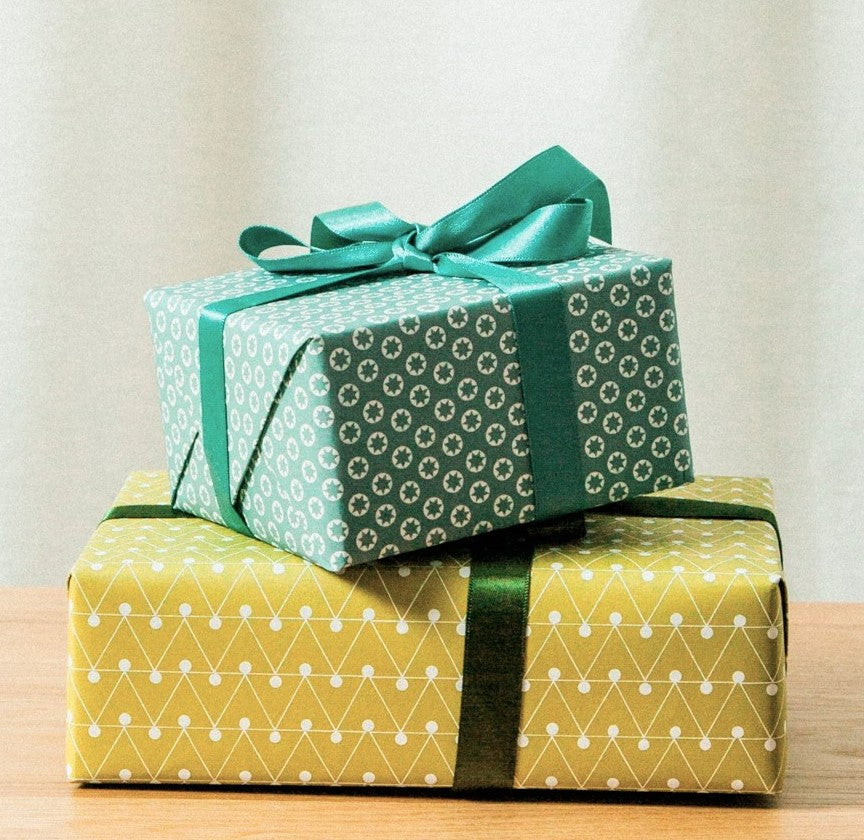 wrapping paper with abstract triangle and dot pattern in mustard and white, wrapped with green ribbon